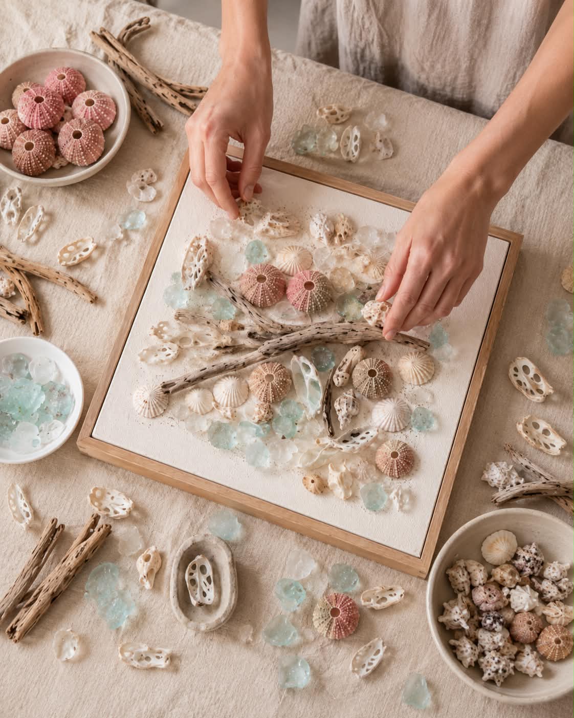 Ocealia arranging shells, sea glass and driftwood on a framed canvas in her studio